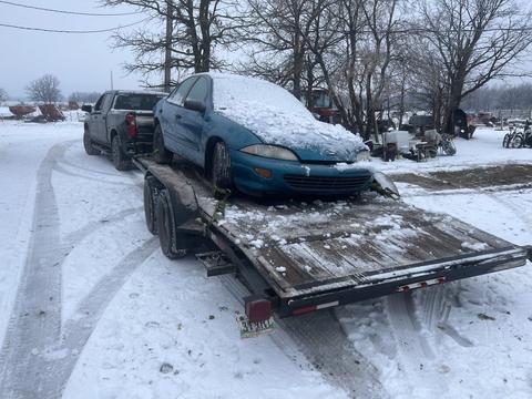 Snow-Covered Car on Trailer at Scrap Metal Recycling Yard